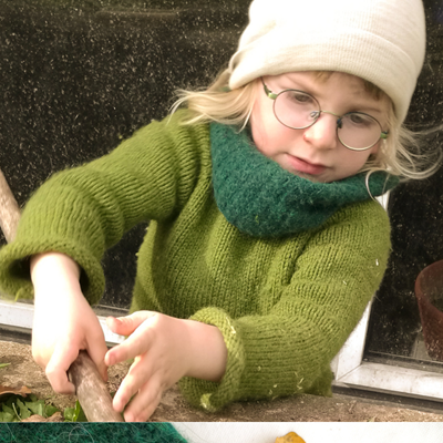 Ein Kind mit Brille und einem grünen Strickpullover samt passendem Schal hantiert draußen neugierig mit einem Stock.
