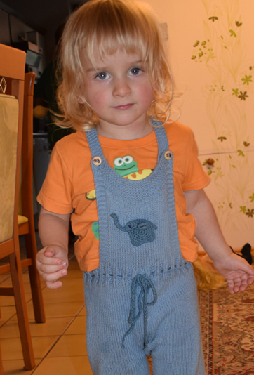 Ein Junge trägt eine gestrickte Latzhose, verziert mit einem gehäkelten Elefanten-Aufnäher