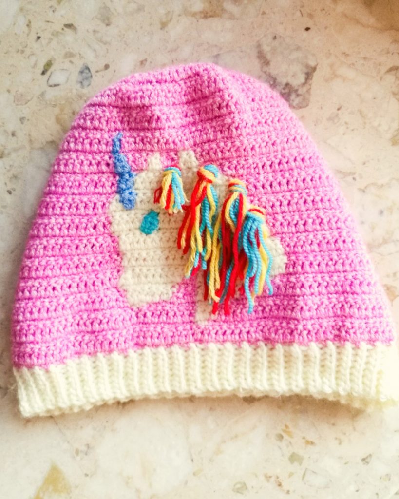 Eine rosa Häkelmütze für Mädchen mit einem niedlichen Einhorn darauf.